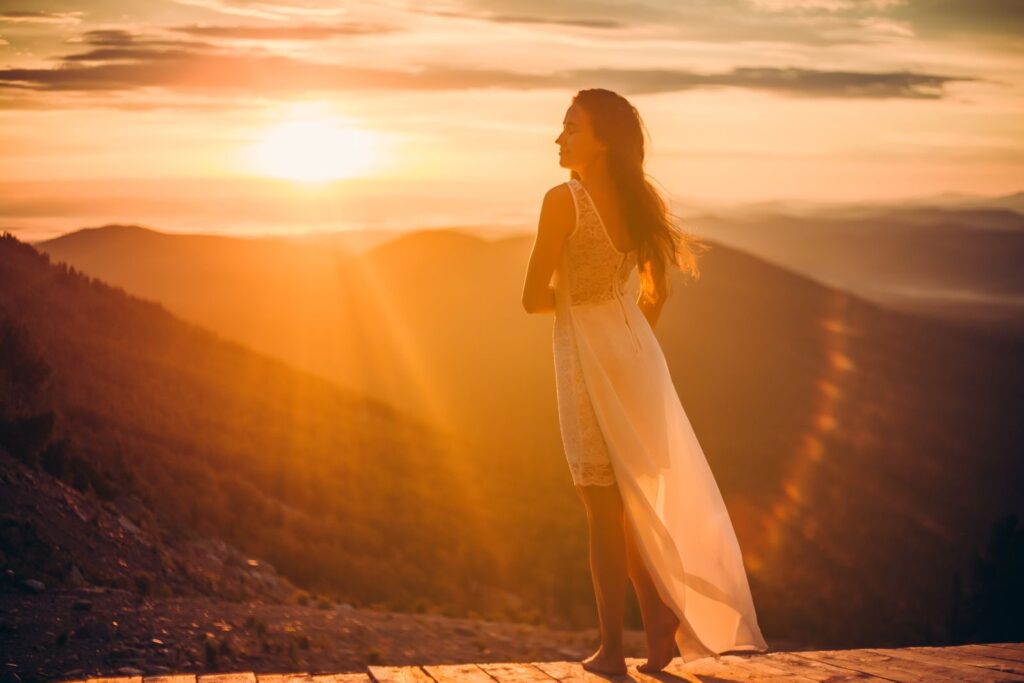 A woman in a flowing dress admires the sunset from a mountain top.