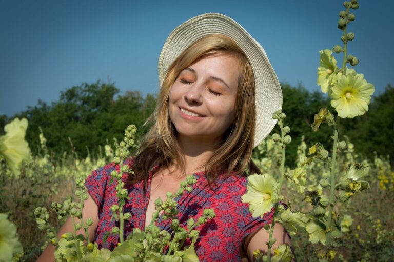 A woman enjoys a sunny day in a field of yellow flowers, eyes closed in tranquility.