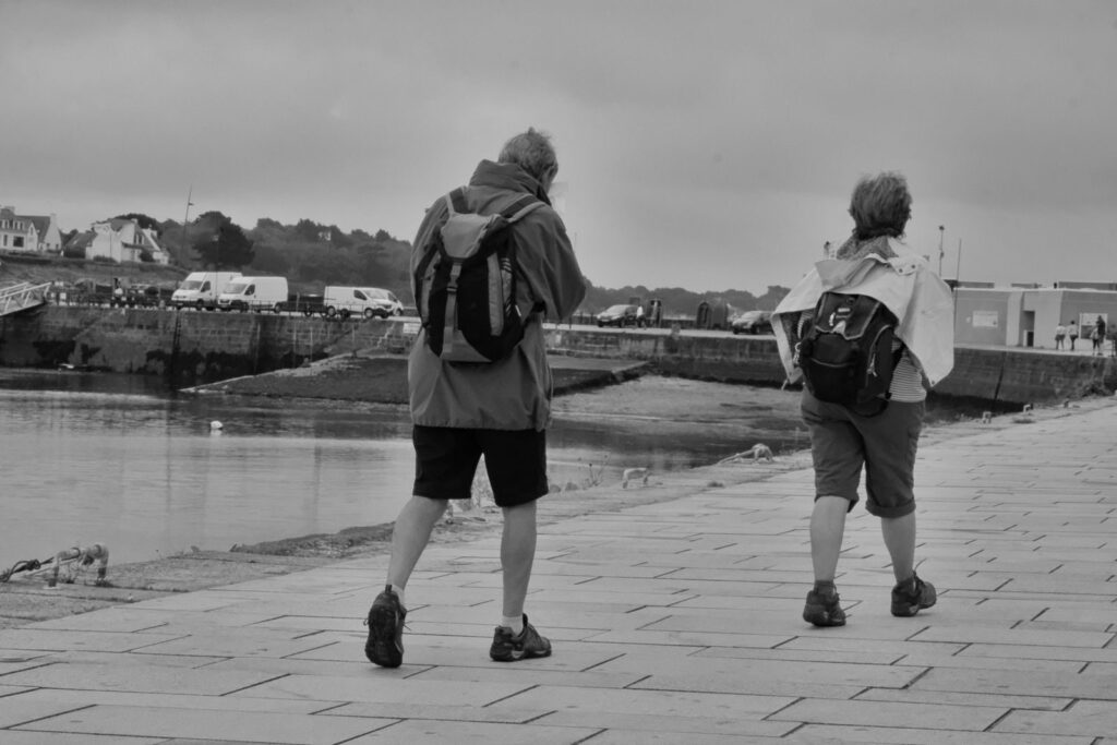 Two adults walking along a scenic waterfront pathway under a cloudy sky.
