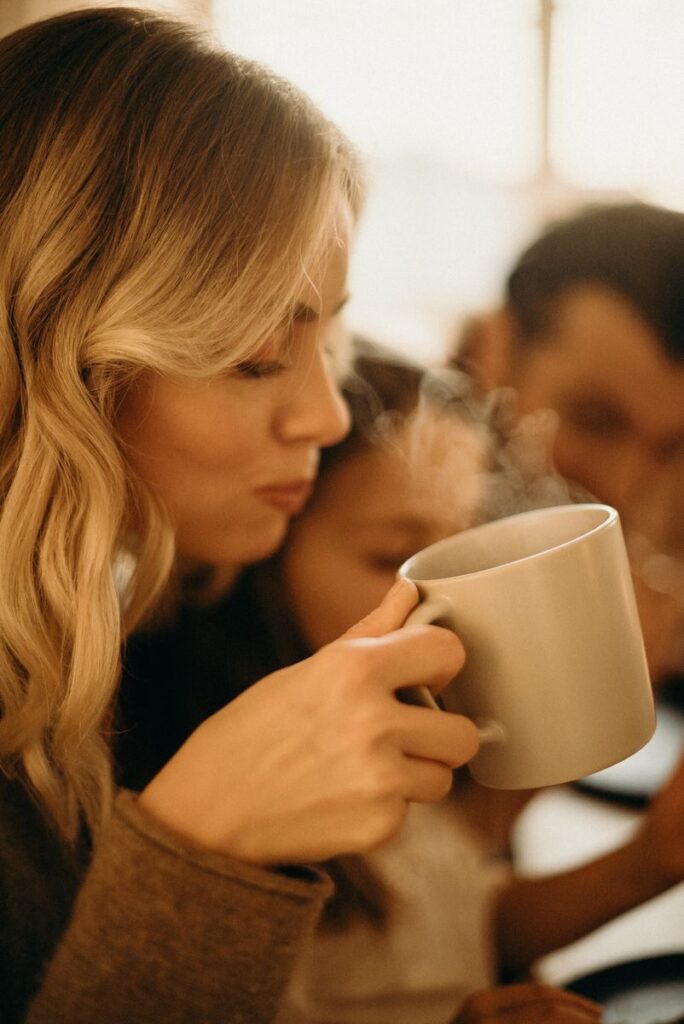 A woman enjoys a steaming cup of coffee indoors with family, capturing a serene moment.