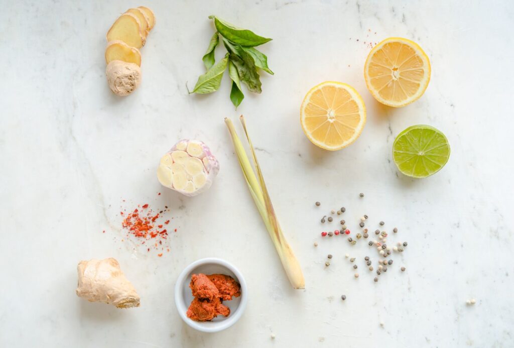 Top view of fresh ingredients including ginger, garlic, lemon, and spices on a white background.