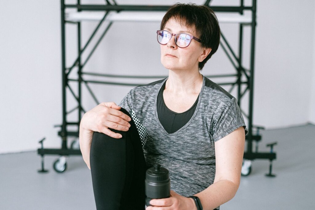 Senior woman resting during workout with water bottle indoors. Stay healthy and active.