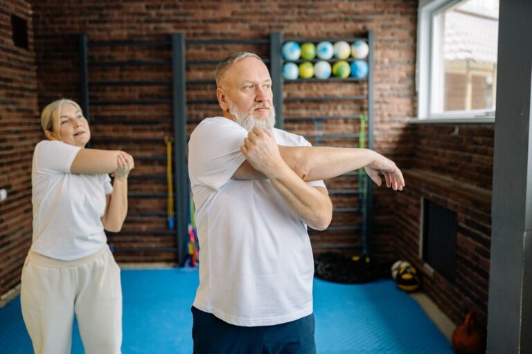 Elderly couple performing arm stretches in home gym to promote wellness and fitness.
