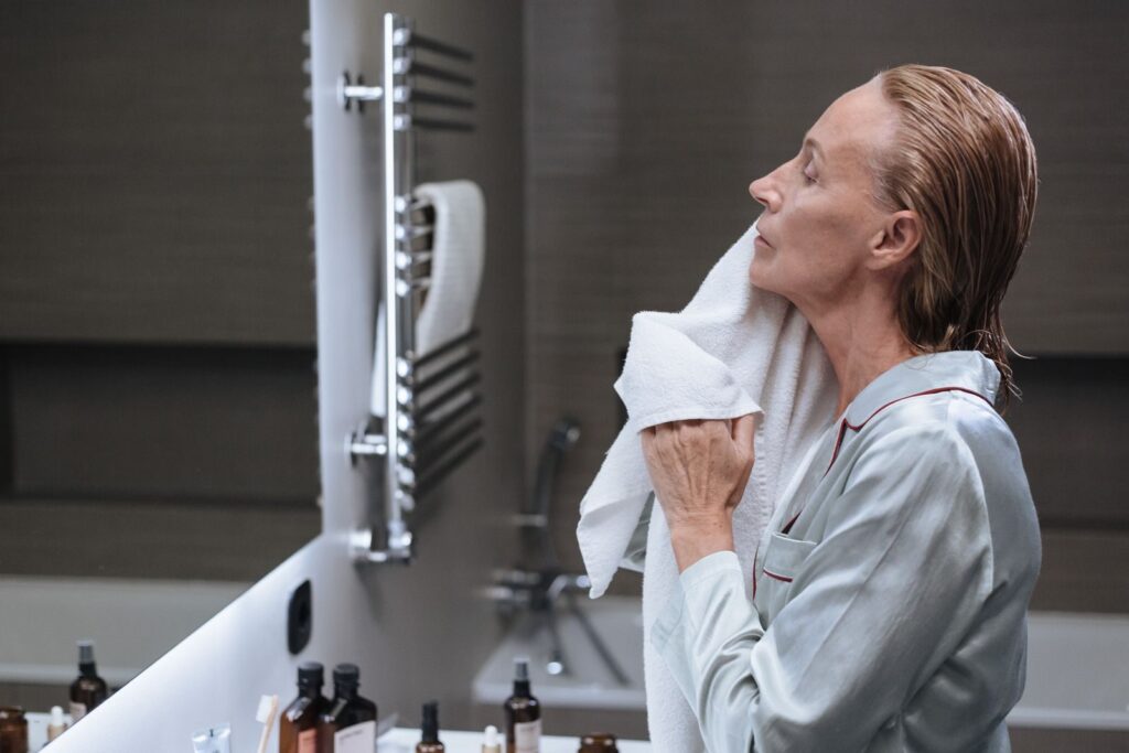 9 Habitudes Pour Réduire l’Apparence des Cernes au Quotidien | Santé et bien-être Senior woman in a bathroom, drying her face with a towel during her morning skincare routine.