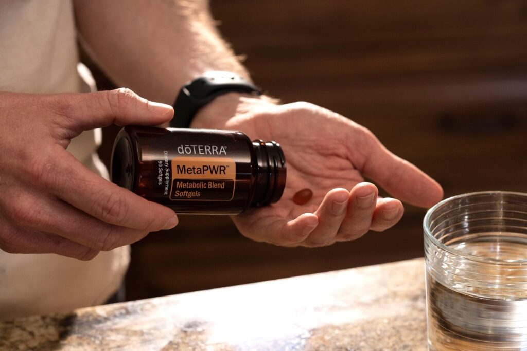 7 Étirements Pour Améliorer la Mobilité du Genou | Santé et bien-être Hand holding MetaPWR metabolic blend softgels next to a glass of water.