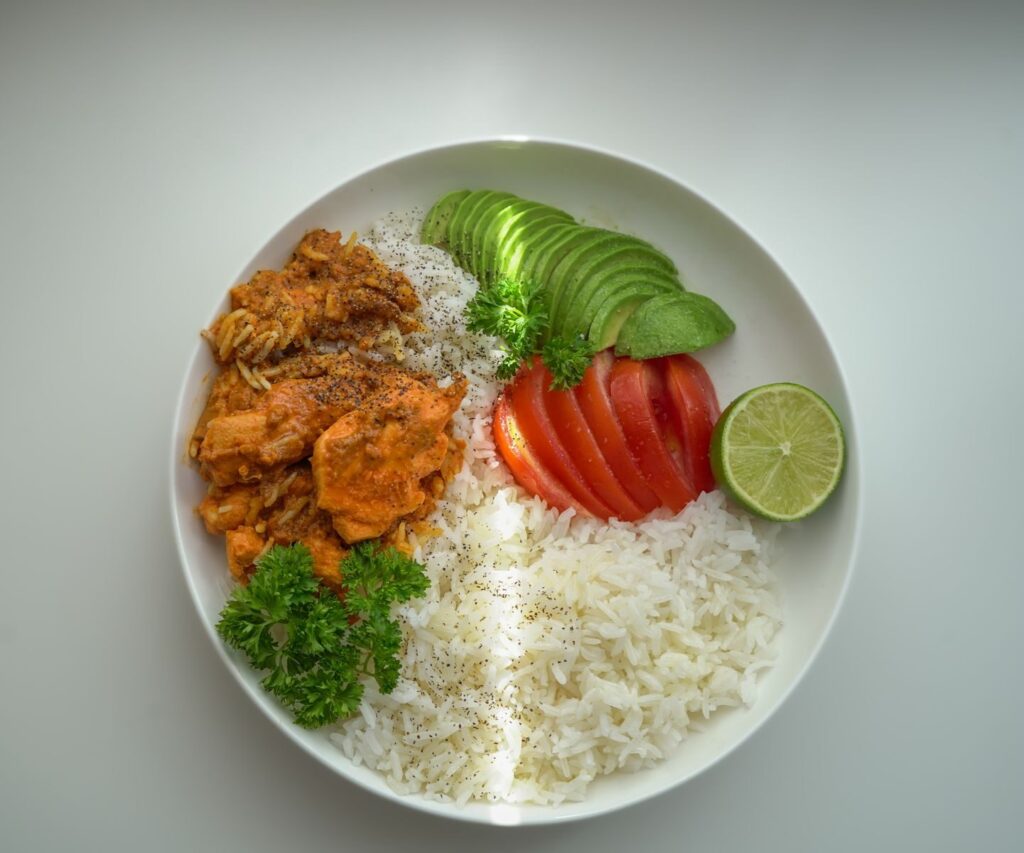 10 idées de repas équilibrés pour une semaine saine | Santé et bien-être A colorful rice bowl with avocado, pork, tomato, and lime, perfect for a fresh meal.