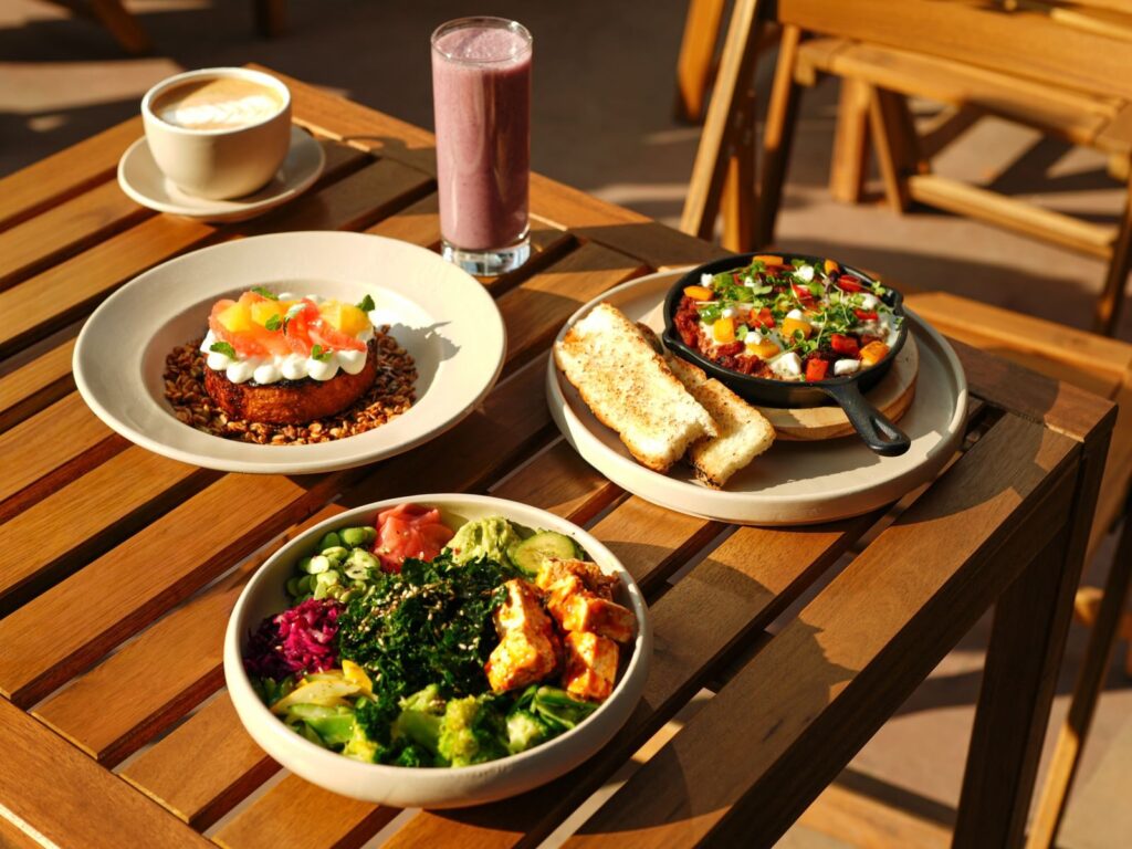 15 Aliments Riches en Protéines Pour les Sportifs d’Endurance | Santé et bien-être A vibrant set of healthy dishes including a smoothie and coffee on an outdoor wooden table.