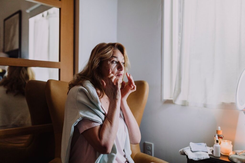 9 Habitudes Pour Réduire l’Apparence des Cernes au Quotidien | Santé et bien-être A woman applies skincare while seated in a cozy, well-lit room, embodying a serene lifestyle moment.