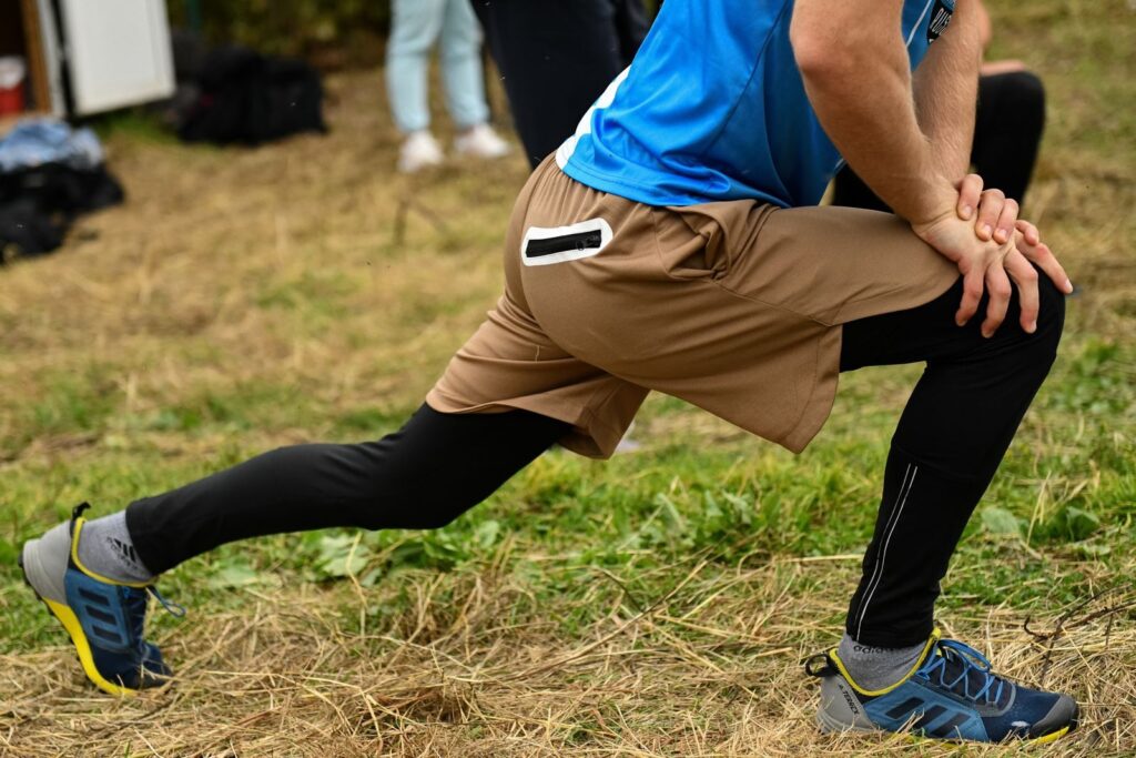 7 Étirements Pour Améliorer la Mobilité du Genou | Santé et bien-être Close-up of a man stretching outdoors in sports attire, focusing on leg muscles and athletic shoes.